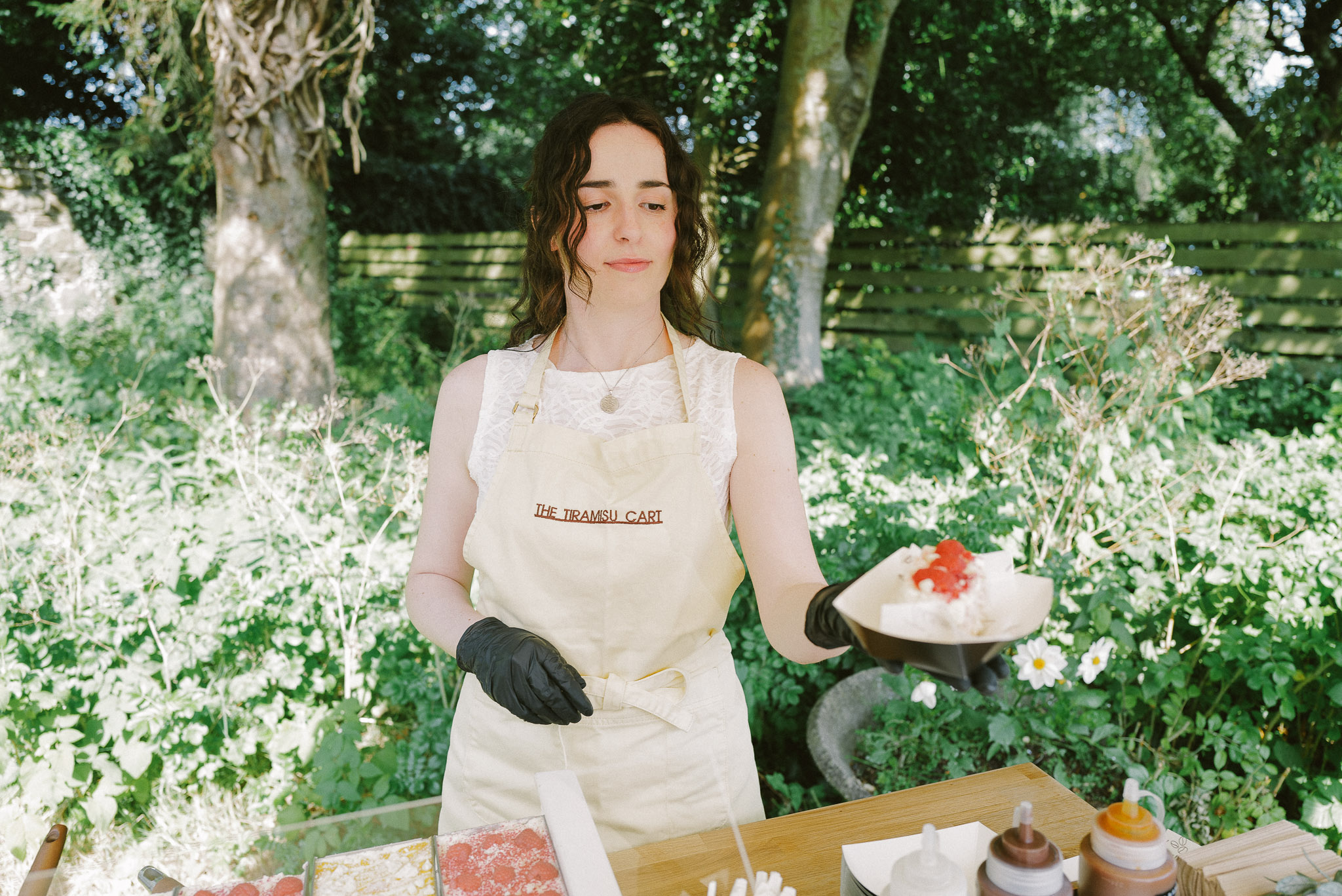 A server holding a fresh slice of tiramisu at the cart